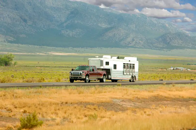 A truck pulling a horse trailer heads down a scenic road.