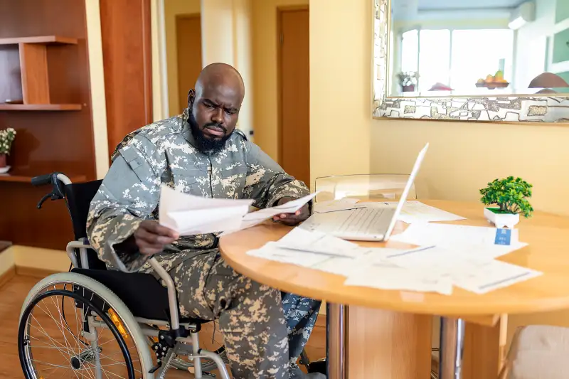 Disabled Veteran US Marine Soldier in Wheelchair. Worried African Veteran in Wheelchair is Looking at Financial Bills at the Home