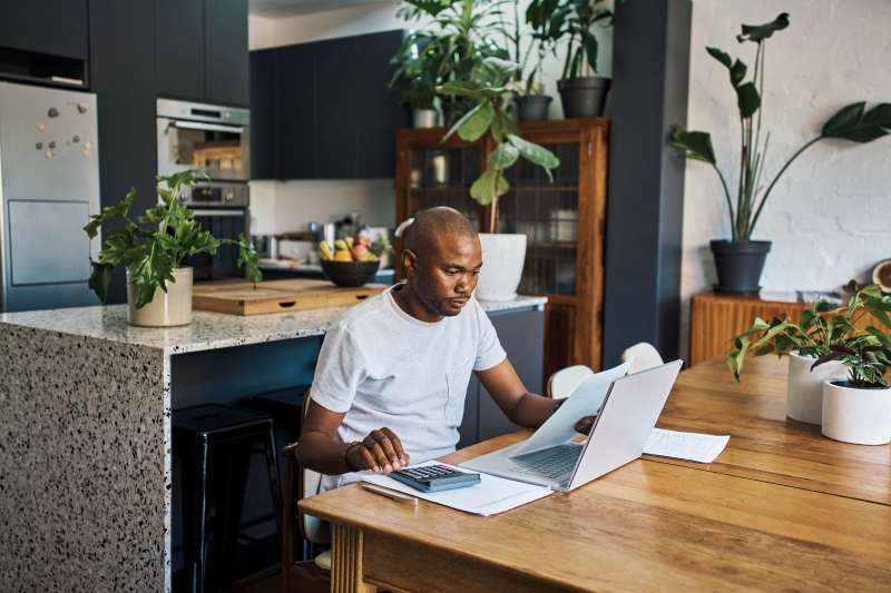 Budget, accounting and businessman in his home with laptop and paperwork for financial planning, document or profit review. Black man remote work from home with finance analysis of bills or bank loan