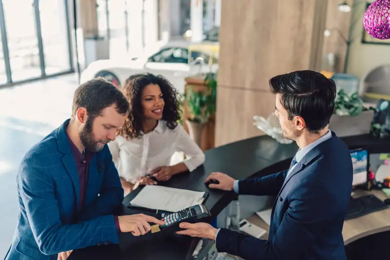 Young family in the showroom paying with credit card for buying new car