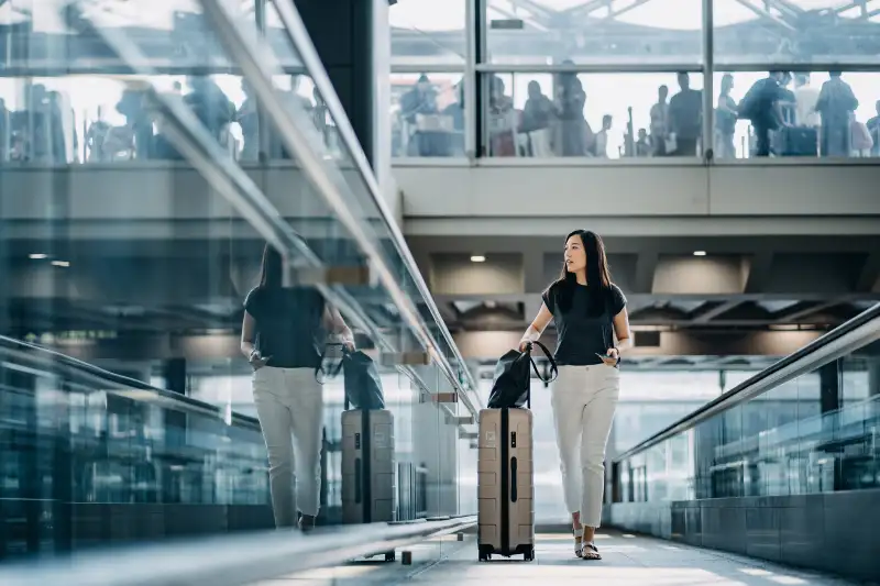 Young Asian woman with passport carrying suitcase walking in the airport concourse
