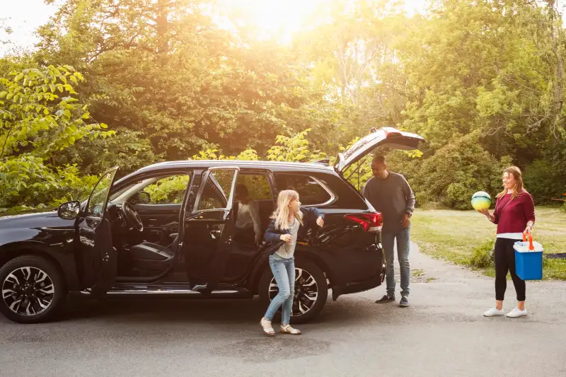 Family by black electric car against trees at park