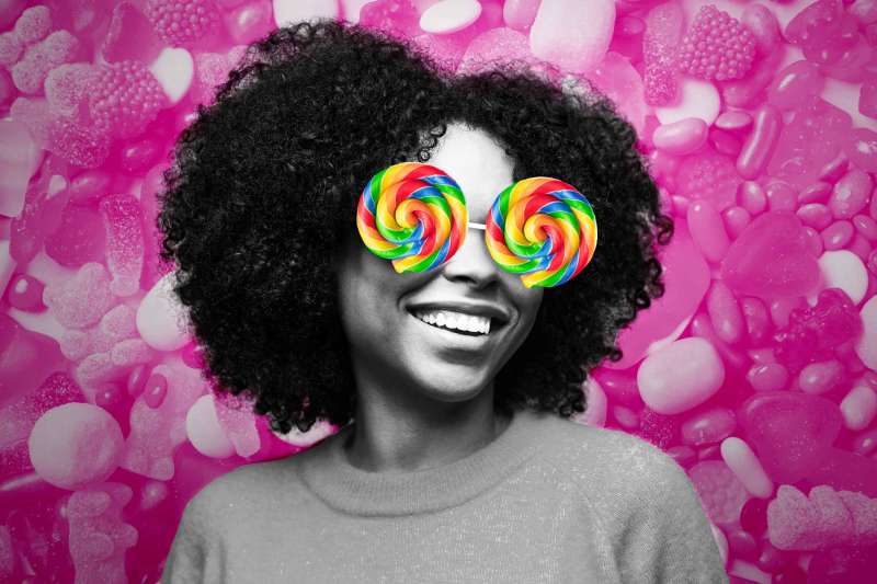 Smiling Person With Lollipop Shaped Sunglasses In Front Of A Candy Filled Background
