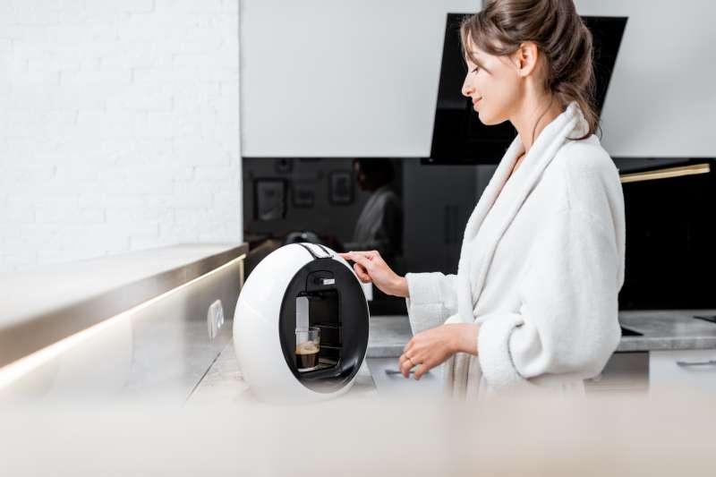 Young woman in bathrobe making coffee with a coffee machine on the kitchen at home