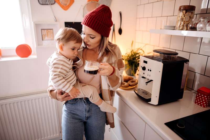 Mother with her son in her arms makes morning coffee with a coffee machine in the kitchen