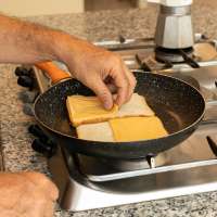 Man preparing cheddar cheese sandwich (for breakfast or snack) on cooking pan.