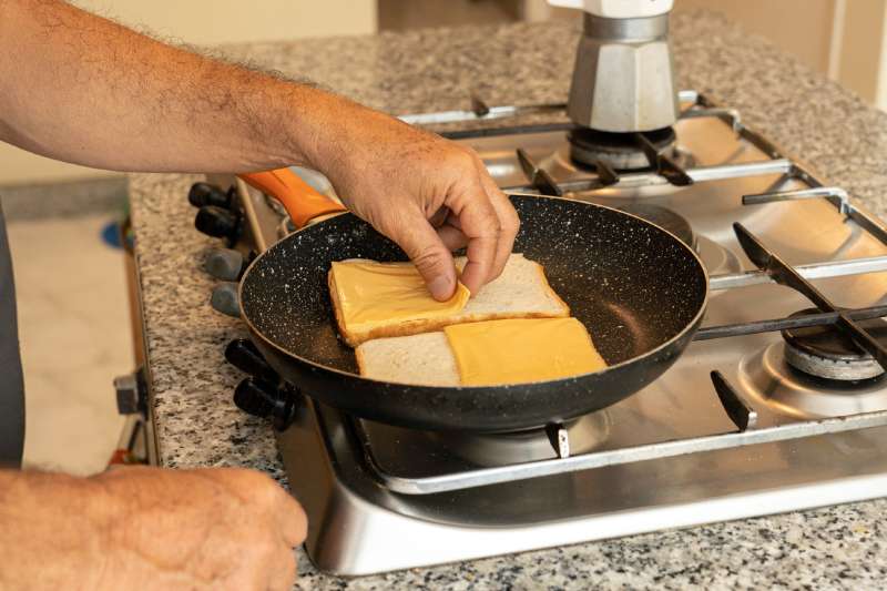 Man preparing cheddar cheese sandwich (for breakfast or snack) on cooking pan.
