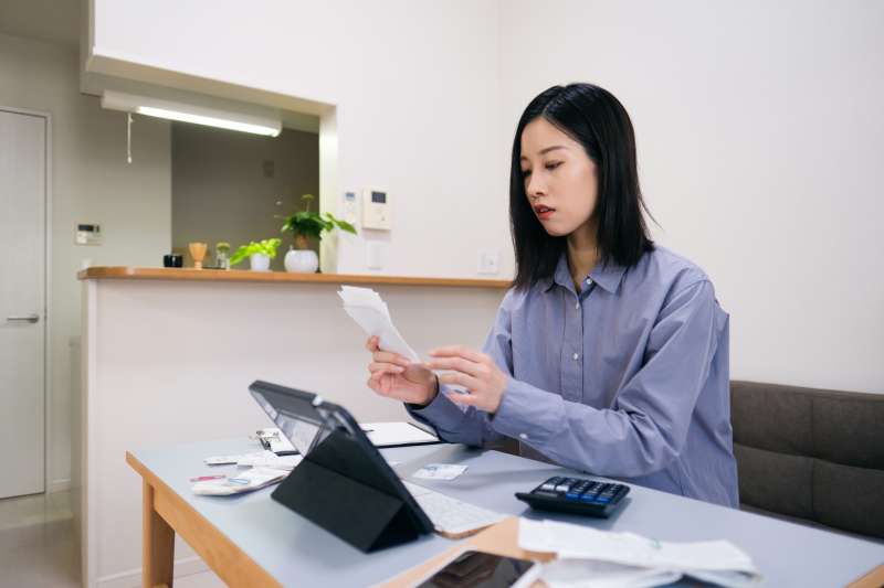 Woman looking over multiple receipts with a calculator and a digital tablet