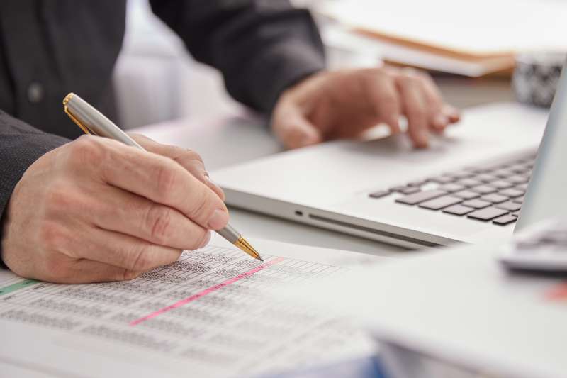 Close-up of a person using a laptop and going over budget sheets