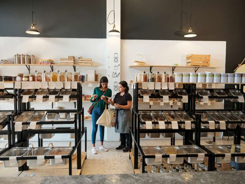 A female costumer standing next to a shopping assistant and looking at the products in a zero waste store.