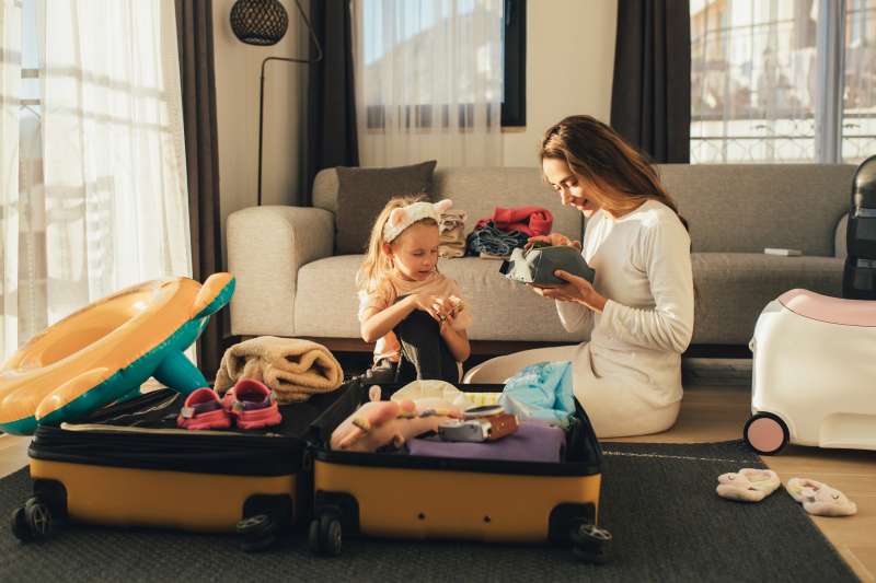Mother and daughter packing their personal belongings into a suitcase in a living room