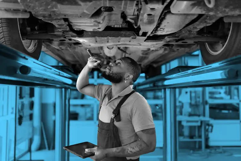 Auto repair specialist examining brake pads of lifted car during inspection.