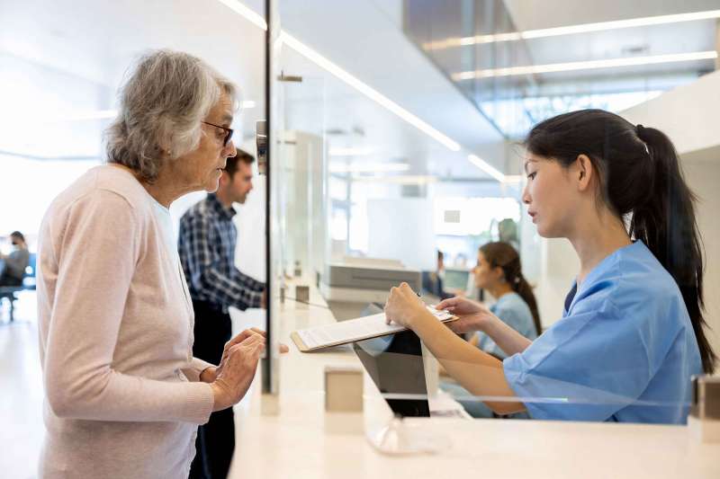 Senior woman registering at the reception of a hospital and nurse asking her to fill a form
