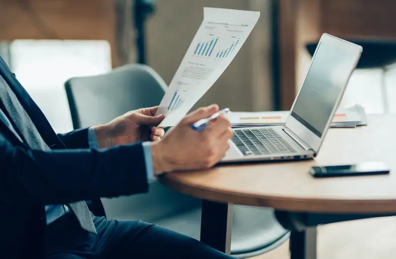 Close-up of a man using a laptop and looking over documents