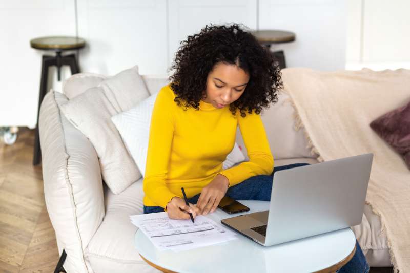 Woman looking over documents with an open laptop next to her