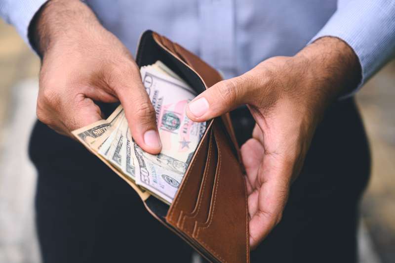 Close-up of a person holding an open wallet with multiple dollar bills