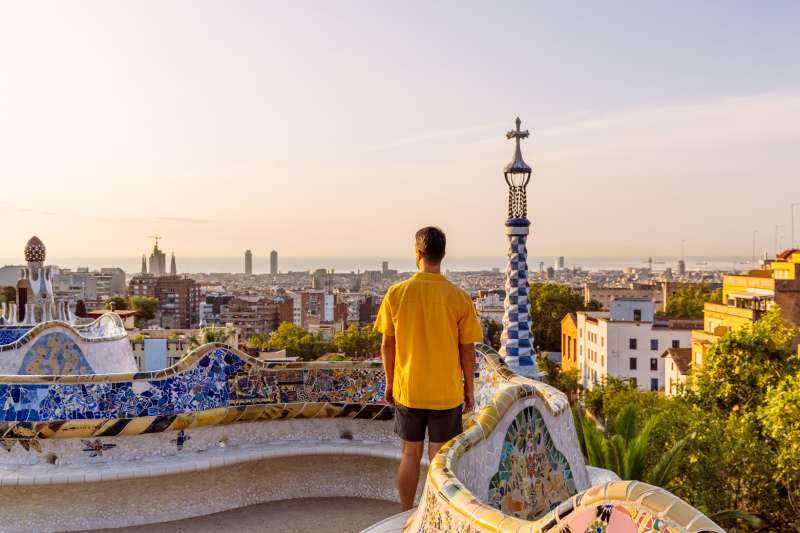 Rear view of a man in yellow shirt looking at Barcelona skyline from above.