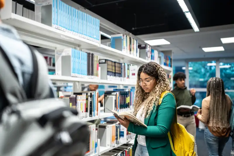 Young student looking through a textbook inside a library