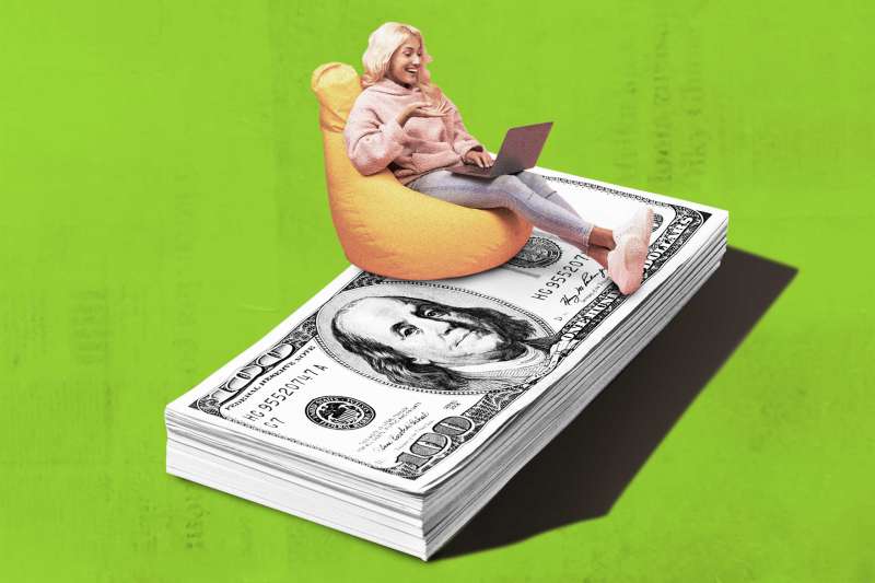 Happy person relaxing in beanbag chair with laptop on top of an oversized stack of cash