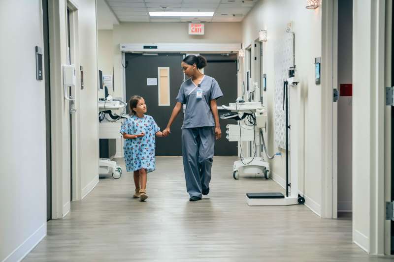 Nurse walking a young patient by the hand in a hospital hallway