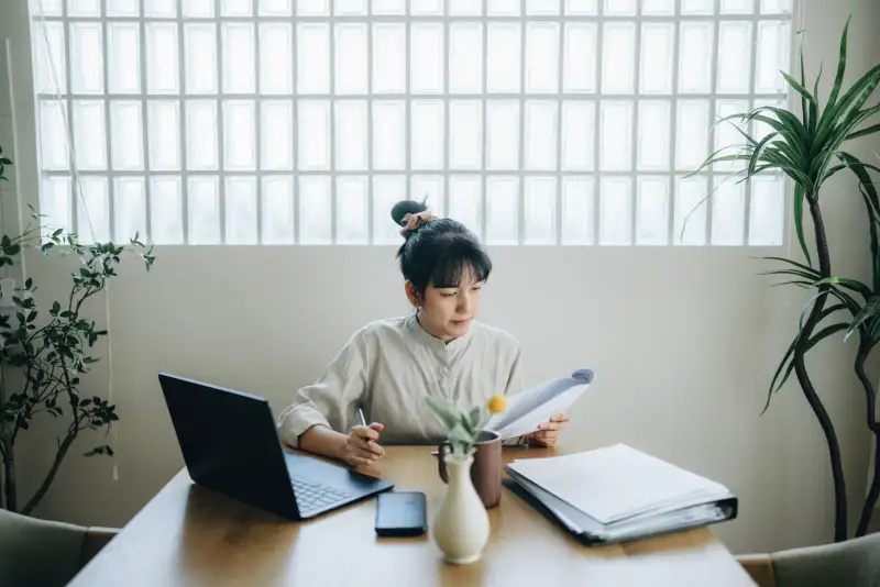 Woman at home looking over some documents and using a laptop