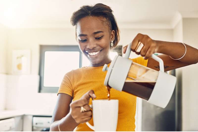 Beautiful, happy and relaxed woman making coffee and pouring hot beverage in cup for morning home kitchen routine