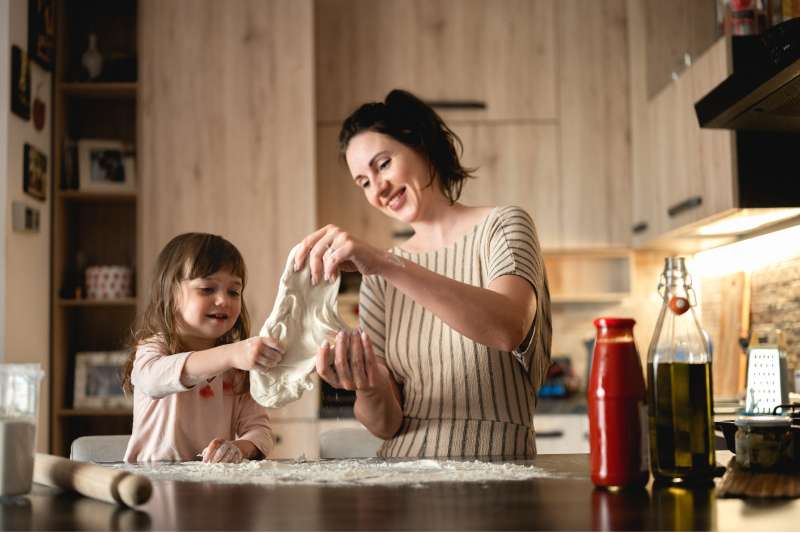 Woman with child preparing dough for homemade pizza.
