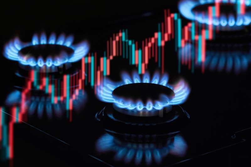 Flaming gas burners on household kitchen stove with an exchange graph of the growth in the cost of natural gas prices