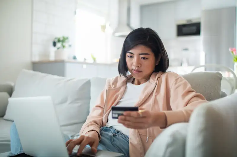 Woman holding a credit card while tipping on her laptop keyboard