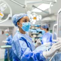 Anesthetist Working In an Operating room Wearing Protective Gear checking monitors while sedating patient before surgical procedure in hospital