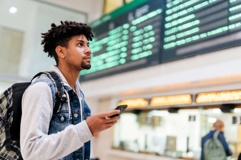 Man at an airport looking looking at the list of destinations holding a cell phone.