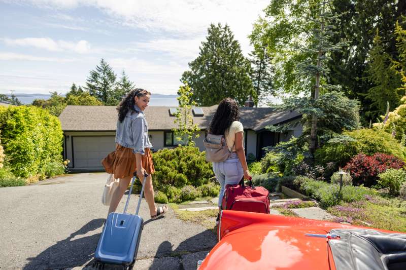 Young women friends with suitcase walking toward sunny vacation house rental