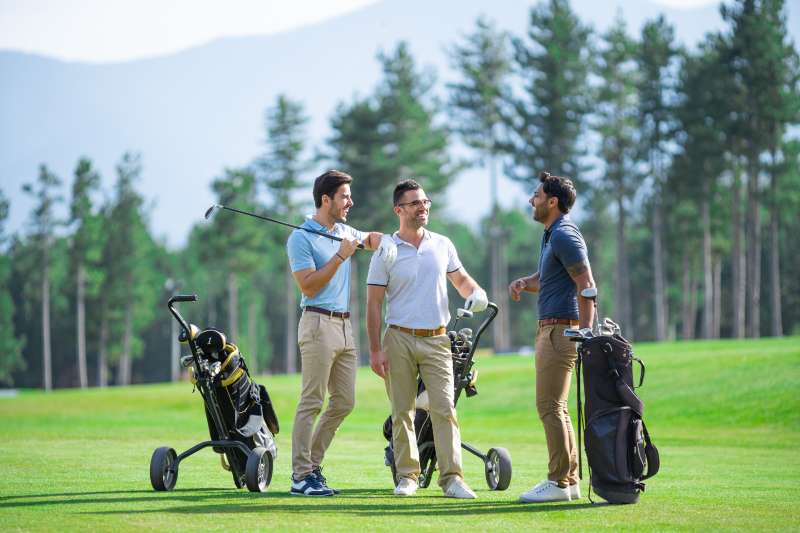 Group of male golfer friends, playing golf on a beautiful sunny day, talking and smiling while standing on golf course