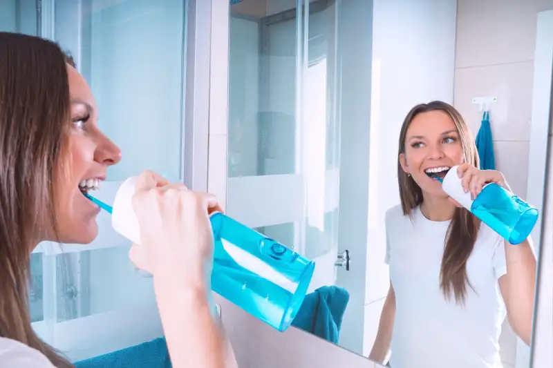 Young beautiful woman with perfect smile using water flosser or oral irrigator while cleaning teeth.