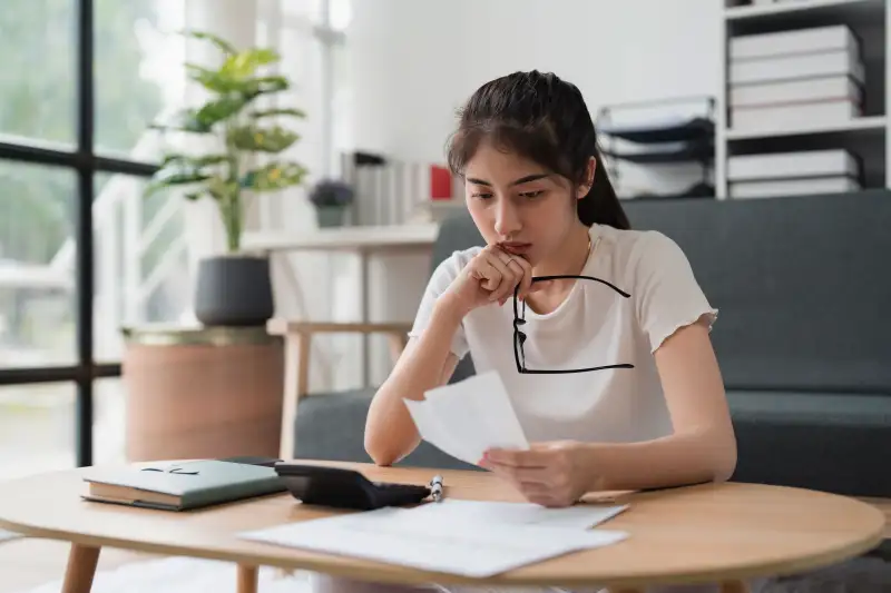 Young woman sitting in her living room looking at paper receipts