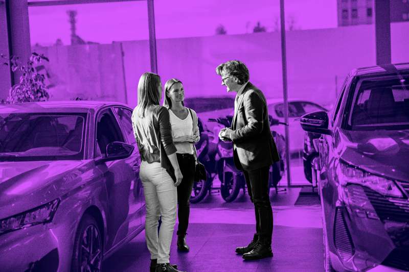 Photo of two women talking to a car salesman in a dealership