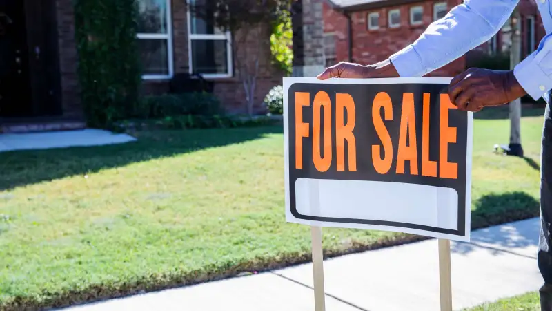 Person sets up  For Sale  sign outside a house