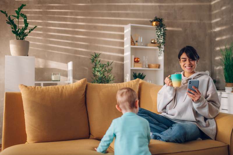 Mother playing and bonding with her child son and using smartphone at home