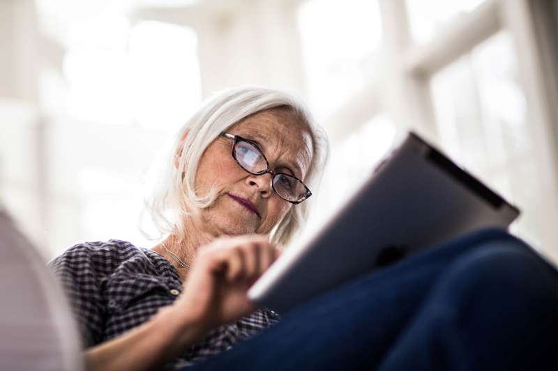 Senior woman looks at life insurance information on tablet.