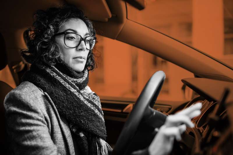 Woman behind steering wheel using phone for navigation