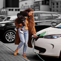 Young mother with child charging electro car at the electric gas station.