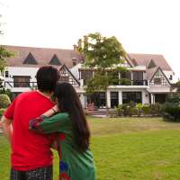 Couple standing with their backs towards camera, looking a big beautiful house in the suburbs