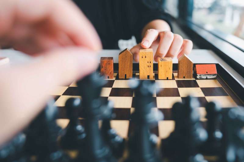 Hand of business man moving chess to Building and house models in chess game