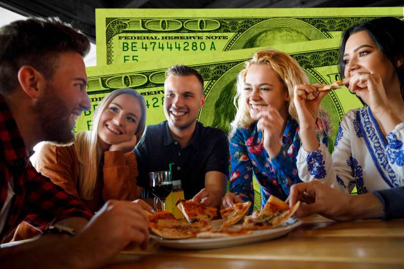 Group of friends sharing a pizza at a restaurant with two hundred dollar bills in the background.