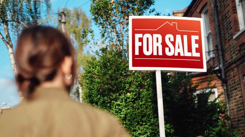 Photo of a person looking at a house's sale sign