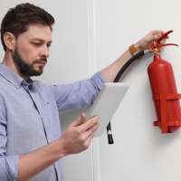 Man looking up instructions on an iPad while holding a fire extinguisher